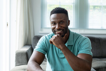 Portrait of smiling afrcian american young man with hand on chin at home