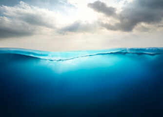 Sunlight shining through the surface of the blue ocean, sea, with a cloudy sky above and dark waters below.