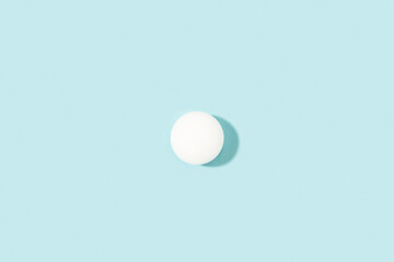 Pelota de ping-pong blanca proyectando sombra sobre un fondo celeste pastel liso y aislado. Vista superior. Copy space