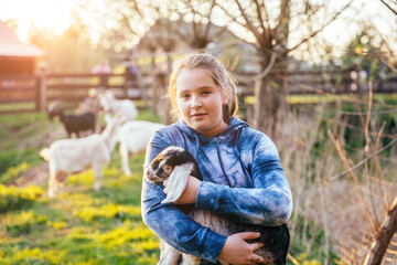Portrait of cute teenager girl with holding goat kid domestic animal at farm in countryside....