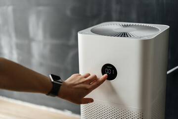 woman's hand presses the touch screen button to start an air purifier in her apartment. Human...