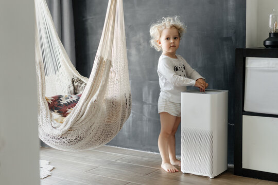 A small child with blond curly hair is enjoying fresh clean air from a dust cleaning system at home. Technology and human health.