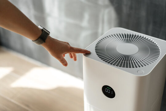 A woman's hand presses the start button of an air purifier in her apartment. Health and technology.