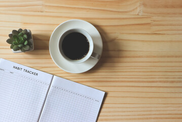 flat lay of habit tracker book, a cup of black coffee and succulent plant pot on wooden table  background with copy space.