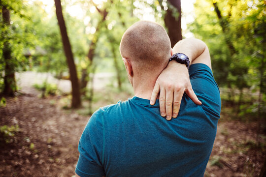 Cropped shot of a man touching his neck while out for a workout in the forest. Shot of a sporty young man holding his neck in pain while exercising outdoors.