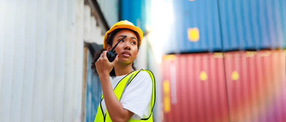 Black female dock worker control loading containers box from cargo at warehouse container yard. Marine and carrier insurance concept. cargo shipping container box in logistic shipping yard