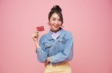 Happy beautiful Asian teen shopaholic women showing credit card isolated on pink background.