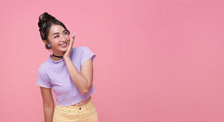 Happy young Asian teen woman looking at copy space on pink background.