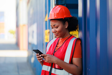 Online working by smartphone. Black female dock worker control loading containers box from cargo at...