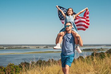 Happy family father and child with flag of America enjoy sunset in nature. The concept of freedom, lifestyle