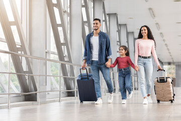 Happy Middle Eastern Family Of Three Walking With Suitcases At Airport Hallway