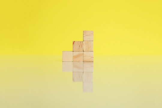 Wooden cubes together arranged in column on yellow background with reflection. Conceptual and symbolic image. Copy space.