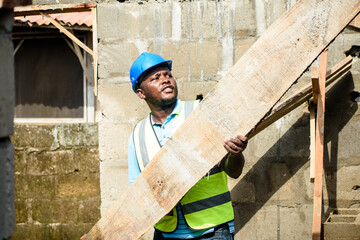 African male construction worker with a helmet working with a plank on a building site in Nigeria