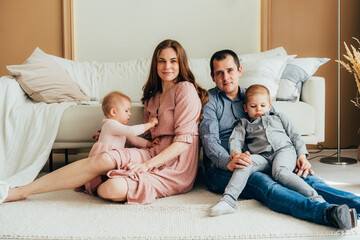 Young happy mom and dad are hugging children sitting on the floor.