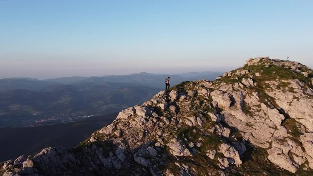 aerial orbital video footage of a man reaching on the summit of a mountain at sunset