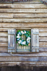 wooden wall with a barred window and a flower wreath on the window