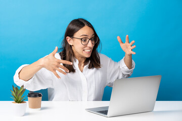 Excited hispanic woman rising hands in front of laptop isolated on blue background.