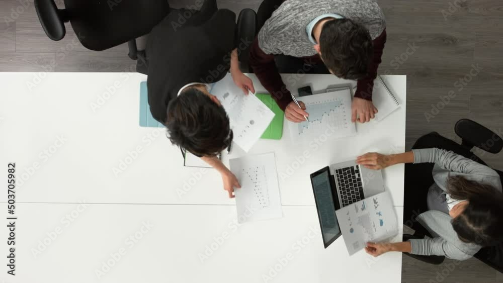 Poster A diverse group of businesspeople planning together in a meeting while reading financial documents. A group of colleagues collaborating in a meeting using a laptop and reading paperwork