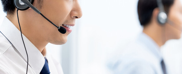 Side view of Asian male consultants in headsets with microphone speaking with clients while working...