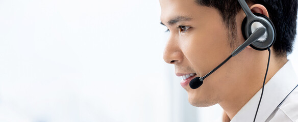 Side view of Asian man worker in headset with microphone speaking with client in white call center banner background with copy space