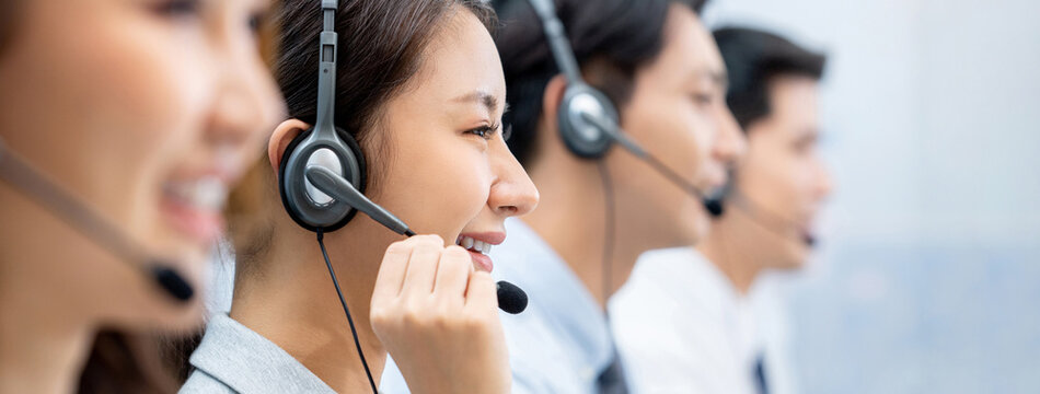 Side view of Asian female operator in headset working in call center office with team