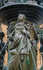 Great close-up view of a bronze figure with a lamb from the famous Fountain of Virtue, representing the virtue patience. The waterspout fountain stands in front of the church St. Lorenz in Nürnberg. - obrazy, fototapety, plakaty