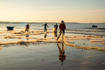 Fototapeta na wymiar Muine, Binh Thuan Beach, Vietnam - October 31 2015: Vietnamese fishermen sort out nets with caught fish in Binh Thuan Beach in sunrise morning at Vietnam