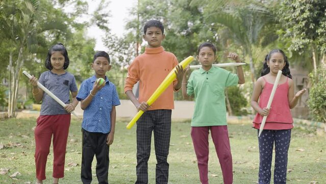 Group of teenager kids with bat, ball and stumps ready for playing cricket by looking camera at park - concept of confident, childhood lifestyle and leisure activities