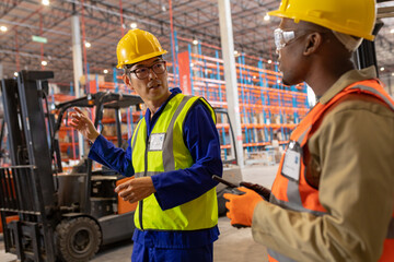 Asian mature man gesturing while talking with african american young male coworker in warehouse
