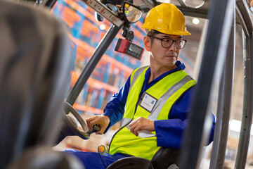 Serious asian mature male worker looking away while sitting in forklift at warehouse