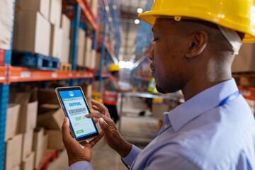 Close-up of african american young male worker tracking shipment over digital tablet in warehouse