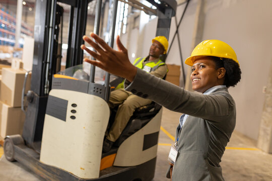 African american young female foreman gesturing while guiding male coworker sitting in forklift