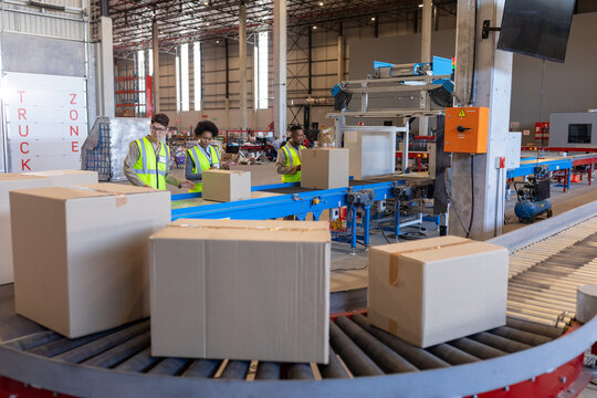 Asian mature man with african american young coworkers processing cardboard boxes on conveyor belt