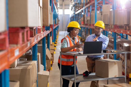 African american young woman and male coworker discussing over laptop while standing amidst shelves