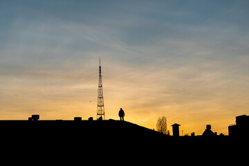A silhouette of two men working on a roof of a building in the city at a sunset time. Golden hour, big tower and residential buildings.