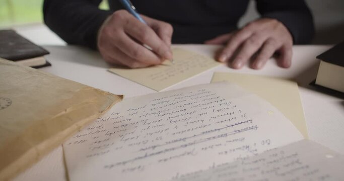 A man writes a letter with a ballpoint pen. Slow camera tilt up and dolly movement. Cinematic mood