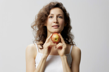 Smiling lovely cute curly beautiful woman in basic white t-shirt pulls apple enjoy healthy food posing isolated on over white background. Natural Eco-friendly products concept. Copy space