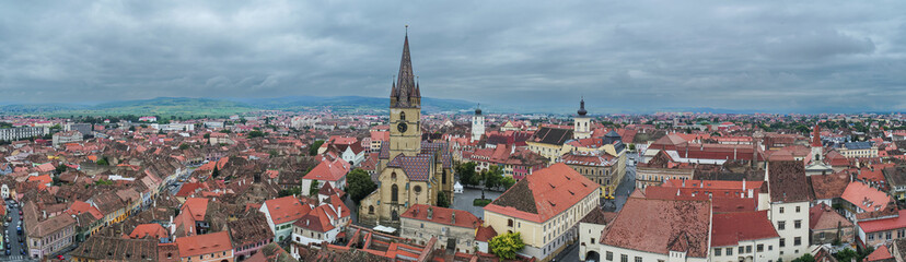 Fototapeta na wymiar Landmarks of Romania. Aerial view of the old center of Sibiu city at the bottom of Fagaras Mountains during a cloudy sky day. Evangelical Cathedral in frame.