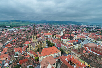 Fototapeta premium Landmarks of Romania. Aerial view of the old center of Sibiu city at the bottom of Fagaras Mountains during a cloudy sky day. Evangelical Cathedral in frame.