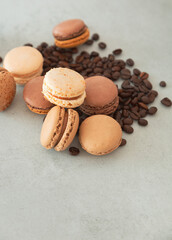 Chocolate, coffee and nut macarons with coffee beans lie on a gray background with copy space. Vertical photo with confectionery - macaron.