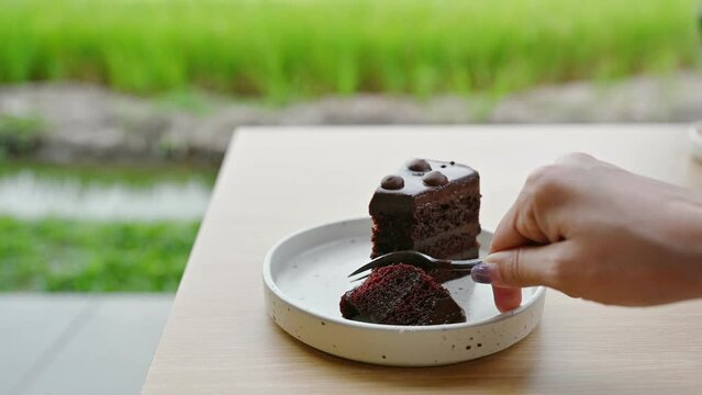 Woman hand using fork cutting dark chocolate cake in ceramic dish