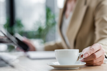 selective focus of white coffee cup near cropped banker on blurred background.