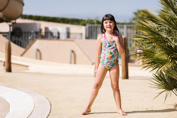 Happy little kid in swimwear standing near pool on sunny day