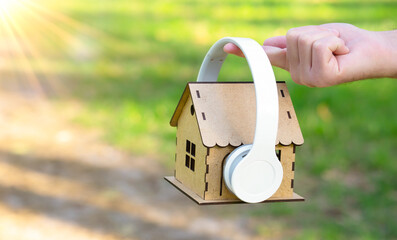 Holding a miniature wooden house with headphones