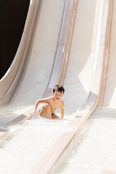 Cute child riding slide in water park on sunny summer day