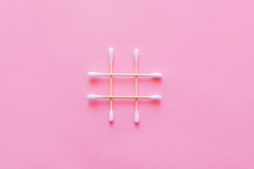 top view of crossed cotton swabs on pink background.