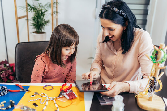 Mother and little preschooler daughters have fun making bracelets at home together