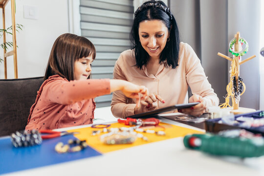 Mother and little preschooler daughters have fun making bracelets at home together
