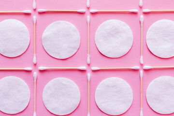 flat lay of white cotton pads and ear sticks on pink background, top view.