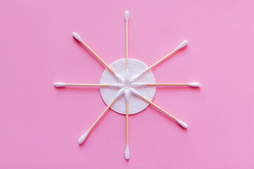 flat lay of cosmetic ear sticks near white cotton pad on pink background, top view.